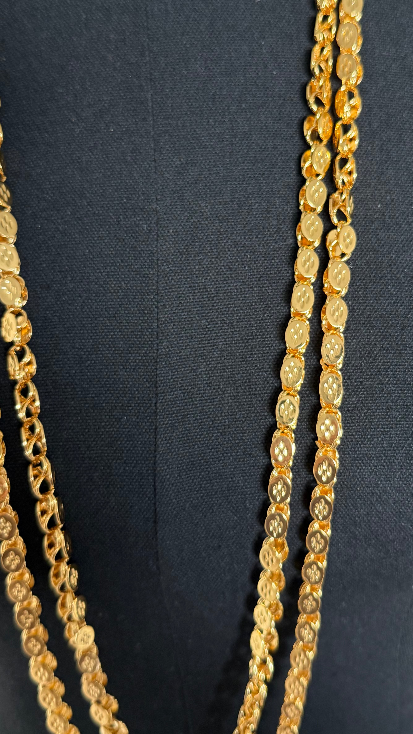 A close-up of a gold-toned chain necklace draped on a black fabric mannequin torso.