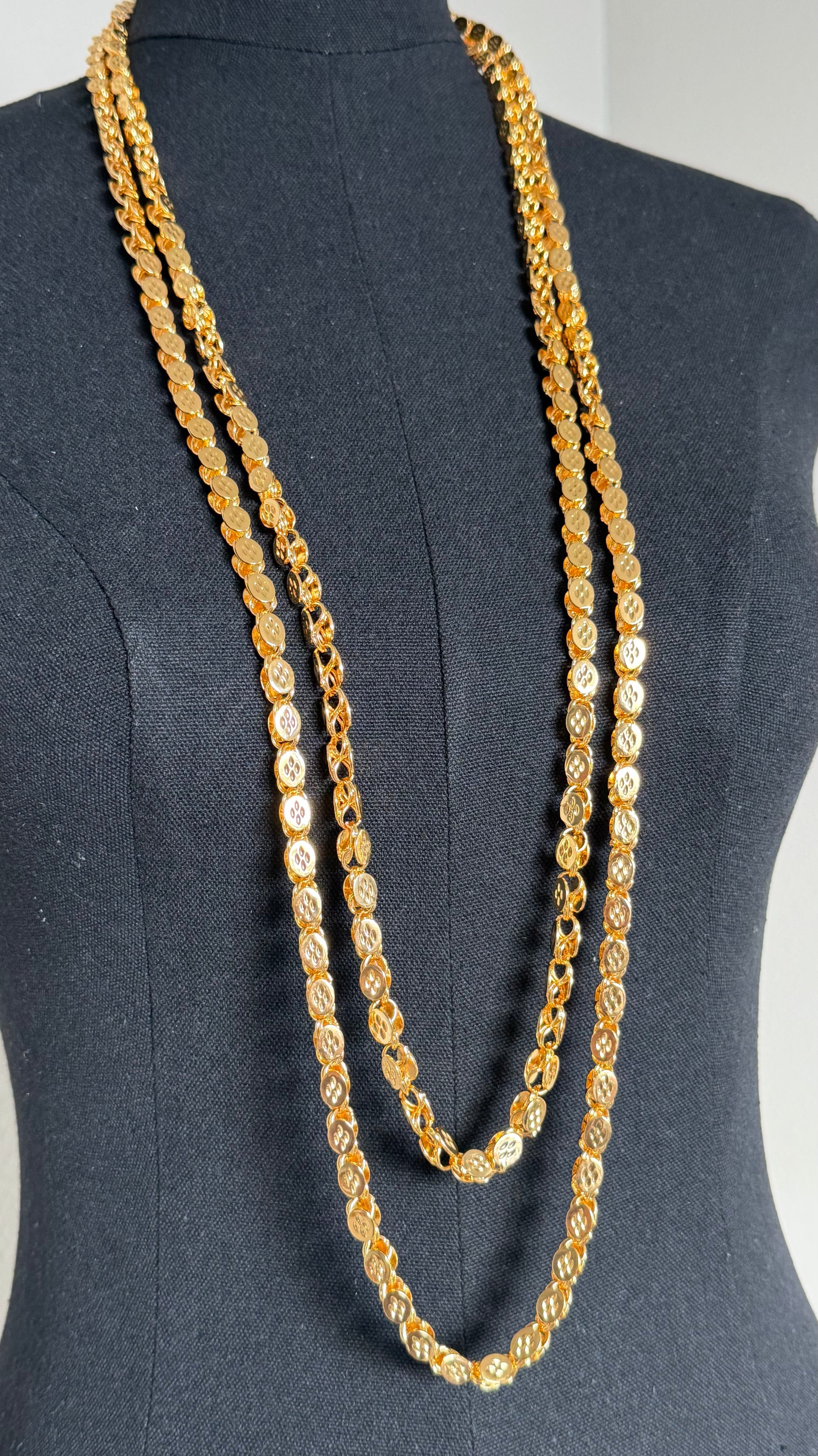 A long layered gold chain necklace displayed on a black dress form mannequin against a light gray background.
